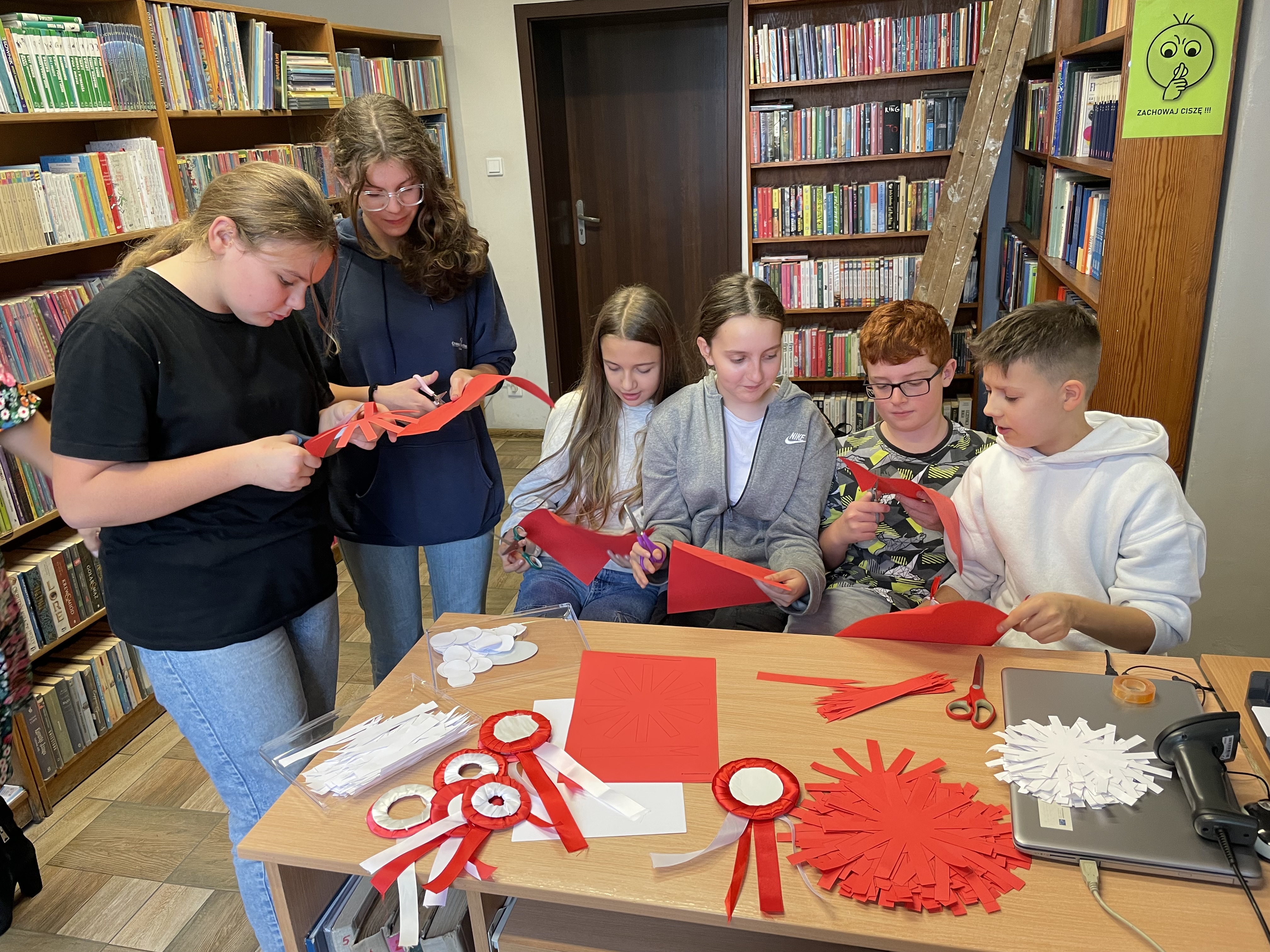 Zdjęcie przedstawia w&nbsp;bibliotece grupę sześciorga uczni&oacute;w wykonujących kotyliony.